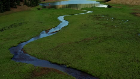 Beautiful-tilt-up-aerial-drone-shot-of-a-stunning-nature-landscape-of-the-Anderson-Meadow-Reservoir-lake-up-Beaver-Canyon-in-Utah-with-large-pine-tree-forest,-a-small-stream,-and-a-grass-field