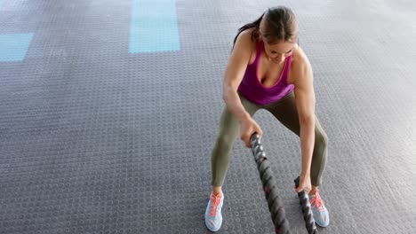 focused unaltered biracial woman exercising with battling ropes at gym, in slow motion