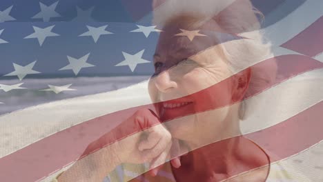 Animation-of-smiling-senior-caucasian-woman-sitting-on-beach-over-flag-of-united-states-of-america