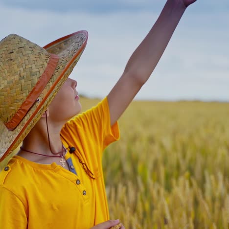 little boy holding wheat ears in hands in a field. kid with rye in hands. straw hat on head. video from a side.