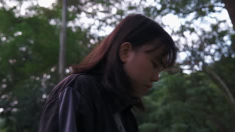 Medium-side-shot-of-young-teenager-girl-in-an-outdoor-park-brushing-her-hair-back-and-leaning-forward