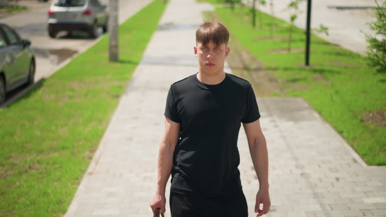 Un hombre blanco camina por una acera soleada de un barrio residencial, lleva una bolsa de lona, con paso relajado y ropa informal, céspedes verdes y coches aparcados a lo largo del camino, la luz cálida y las sombras suaves crean un ambiente reflexivo
