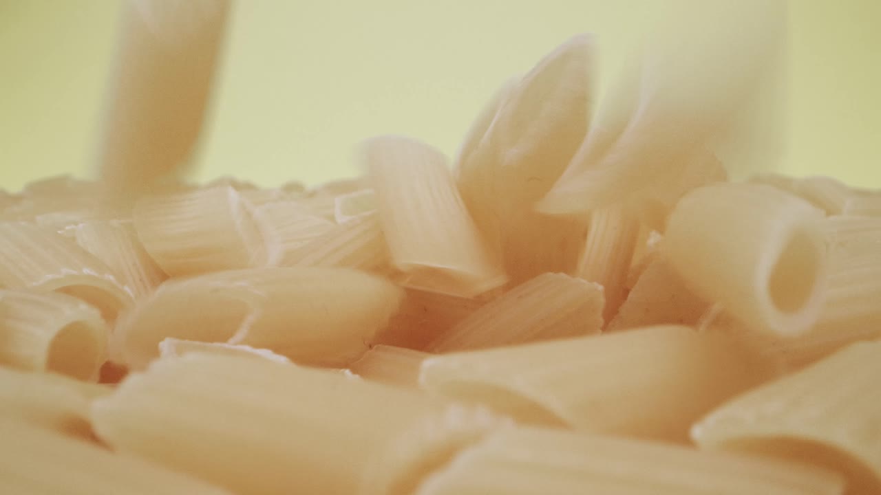 primer plano de la sonda en tiempo real de la caída de la pasta mezze penne rigate sobre fondo amarillo