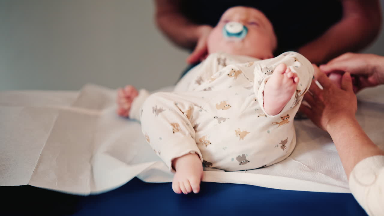 Close up of an infant's legs and feet while caregivers gently reposition the baby during a care or examination session