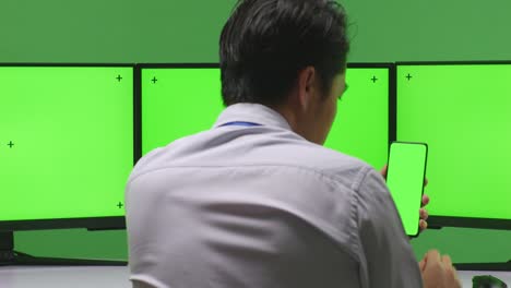 business person using smartphone in front of multiple green screen monitors
