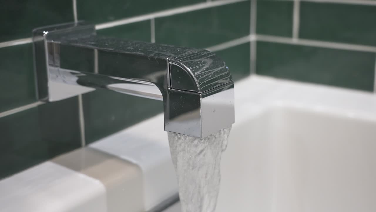 Water beginning to flow out of a silver faucet in slow motion