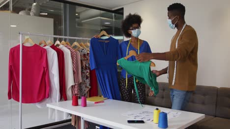 African-american-male-and-female-fashion-designers-wearing-face-masks-in-discussion-at-work