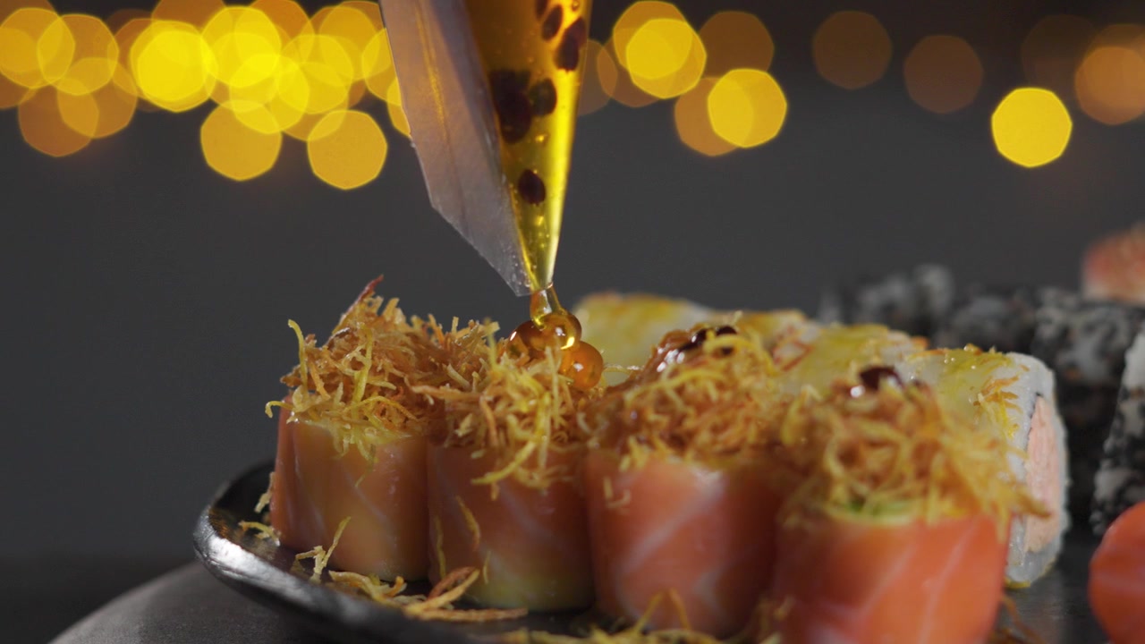 Primo Piano di uno Chef che Versa Salsa Dolce su un Roll di Sushi di Salmone Croccante