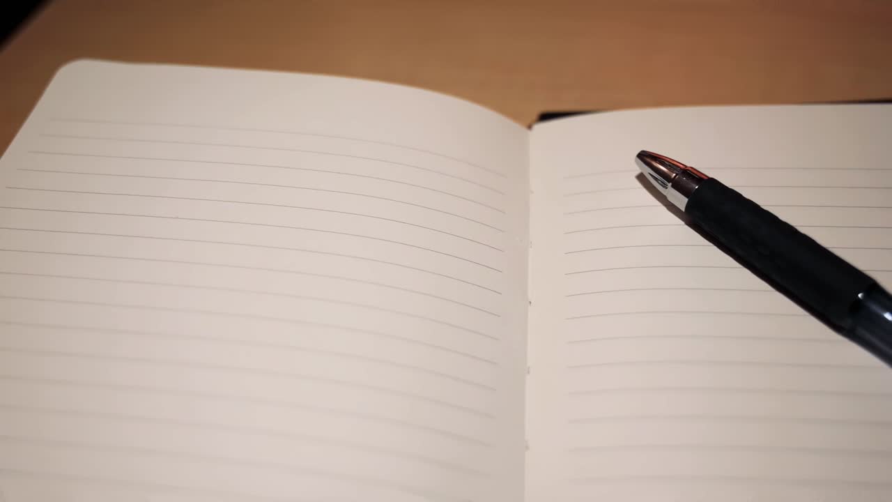 Slow motion high angle tracking shot of pen and journal open to empty page
