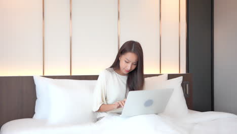 Delightful-young-woman-using-a-laptop-on-her-knees-and-working-online-or-shopping-on-the-internet-and-suddenly-rising-her-arms-in-the-air-with-joy-and-smile-on-her-face