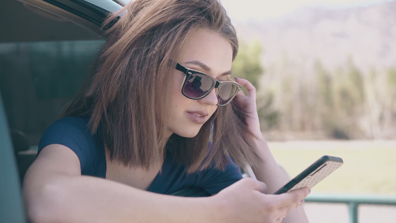 happy girl looks at cell phone sitting inside modern auto