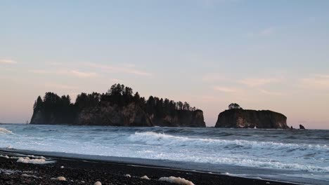 gorgeous tilting up shot the pacific coastline with waves leaving behind sea foam, a beautiful small cliff island, and a colorful cloudy sky during sunset at the famous ruby beach in forks, washington