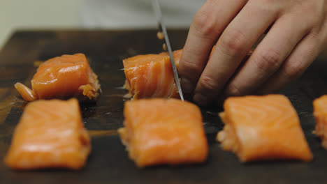 Cierre-La-Cámara-Lenta-Del-Chef-Masculino-Cortando-El-Filete-De-Salmón-En-Trozos-Pequeños-Con-Un-Cuchillo-Afilado