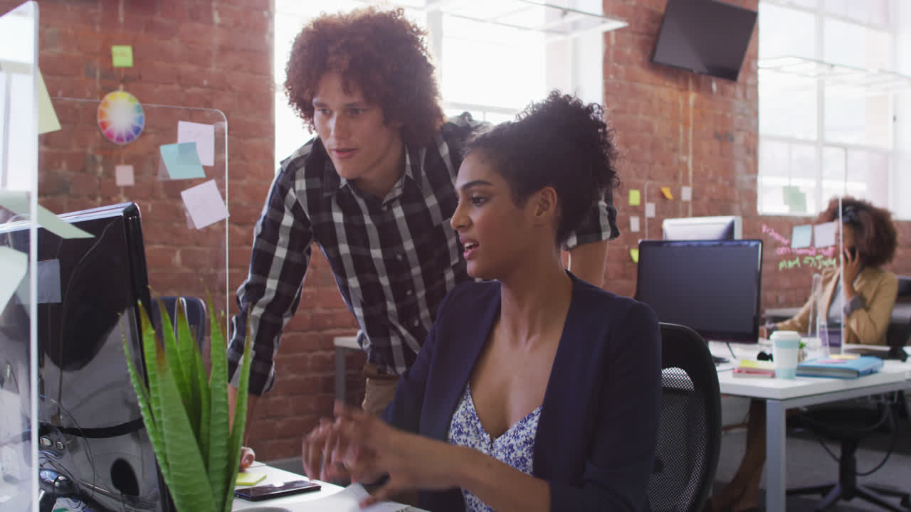 Diverse male and female colleagues discussing over computer screen in office