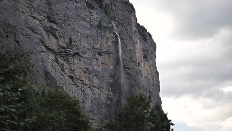 water falling down between the rocks and green trees from a high waterfall in lauterbrunnen in switserland on a cloudy day. wide slow-motion shot