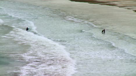 A-pair-of-surfers-move-through-the-water-on-a-beach-on-the-Isle-of-Harris,-part-of-the-Outer-Hebrides-of-Scotland