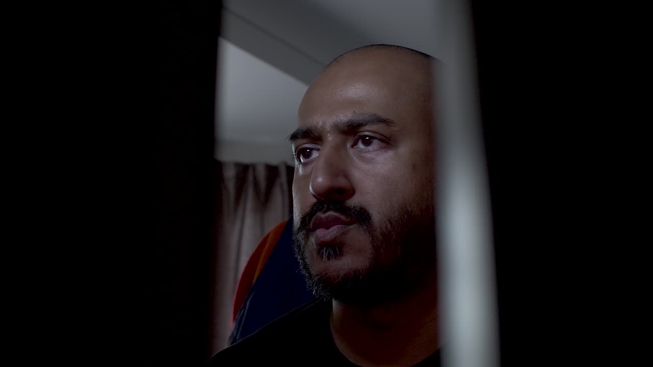 varón indio calvo moviendo la cabeza de lado a lado escuchando música en una habitación con poca luz