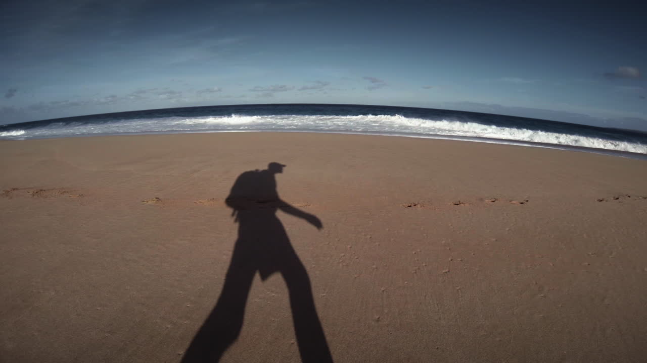 la sombra de un hombre camina por la playa con una mochila