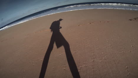 la sombra de un hombre camina por la playa con una mochila