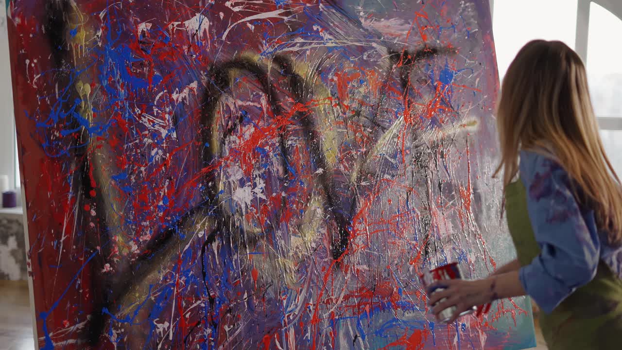 Artist paints on canvas emotionally dipping hands in paints jar and splashing