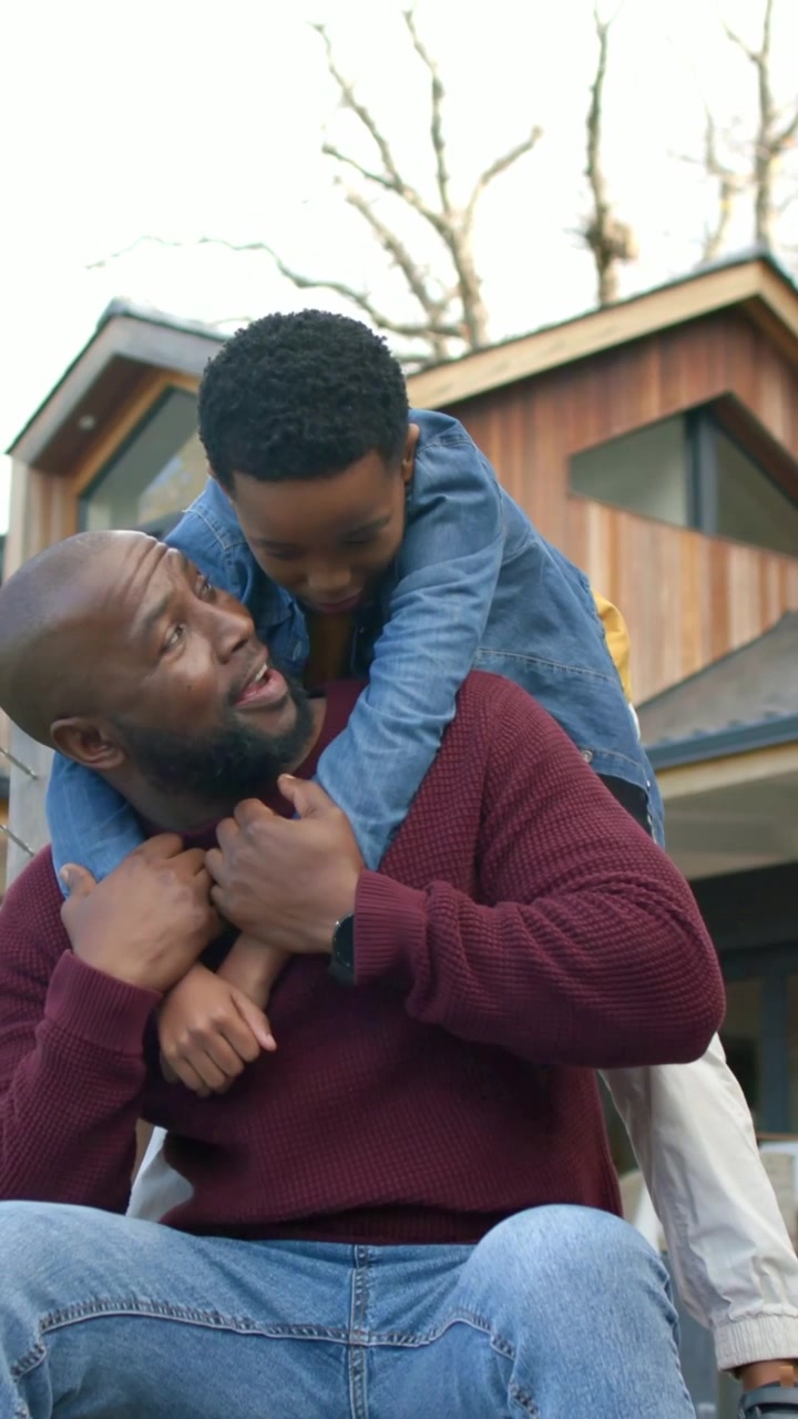 Vertical video: Walking son climbing onto dad's back on porch steps dad steadying hug denim jacket