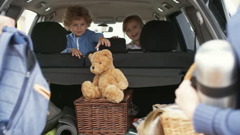 family goes on vacation, parents put luggage in the trunk and little children wait sitting inside the car