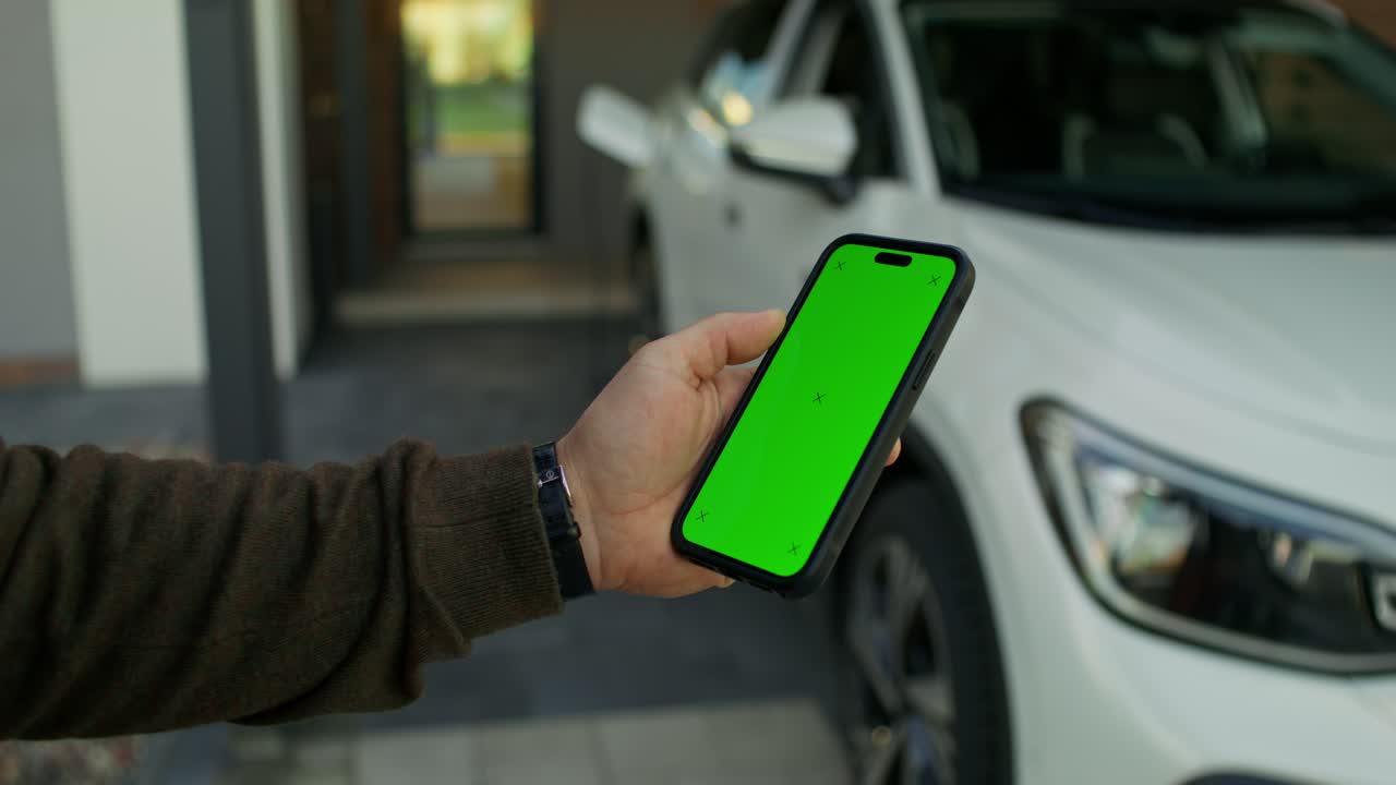 persona sosteniendo un teléfono inteligente con una pantalla verde delante de un coche