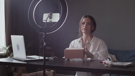 excited young vlogger woman showing to the camera the package she has received and opening the box with scissors