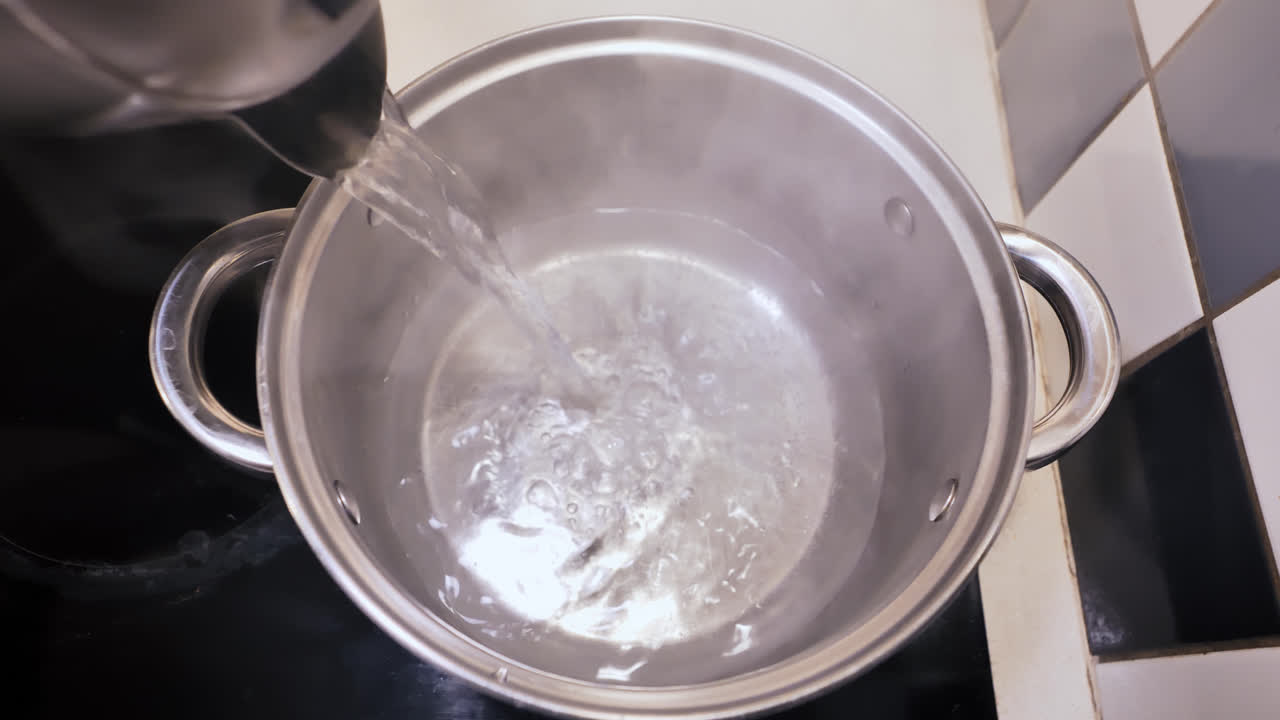 Steam rises as hot water flows into metal pot, quiet kitchen preparation moment