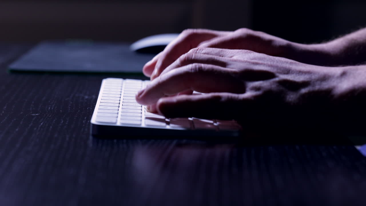 Fingers typing on keyboard, illuminated by the computer screen