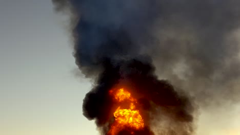 tilt up shot of huge fire causing a massive black cloud of smoke billowing into the sky