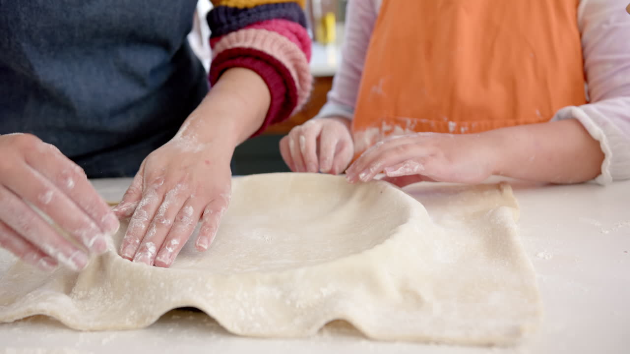 Happy biracial mother and daughter putting dough into cake tin in sunny kitchen