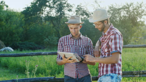 Two-farmers-chat-at-a-fence-of-a-ranch-and-use-a-tablet