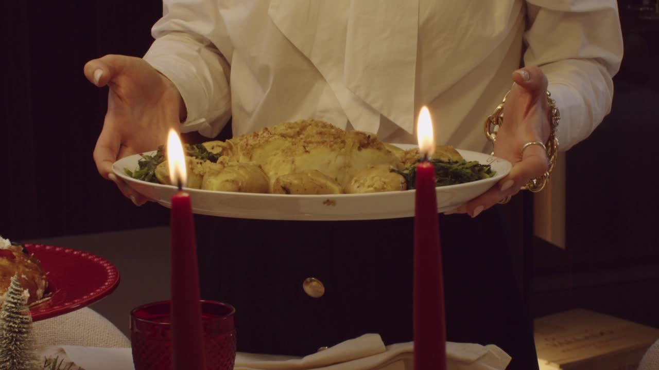 Woman serving roast chicken with greens on a Christmas table lit by red candles