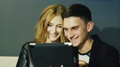 young couple 20-25 years uses the tablet in a cafe they laugh and smile