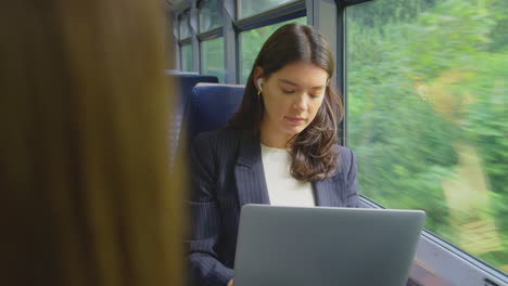 businesswoman with wireless earbuds commuting to work on train working on laptop