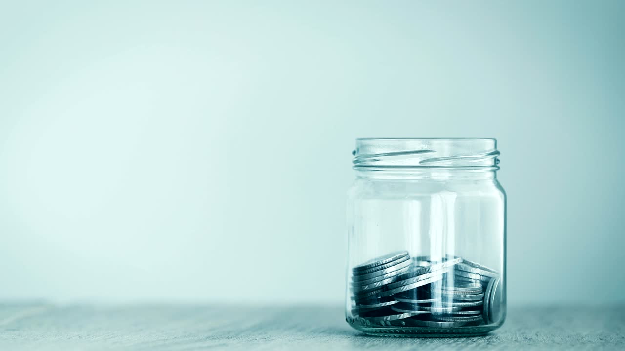 Close up Money coin falling into glass jar , money saving , a donation or business financial growth concept , 4K Dci resolution , vintage retro color tone