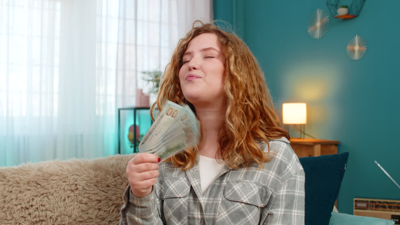 Woman sits on sofa excitedly counting cash dollars celebrating lottery win or unexpected income joy