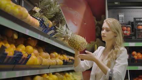 woman choose one pineapple fruit and put it in shopping basket take small pineapple lying near. female customer at fruits and vegetables department of large modern supermarket