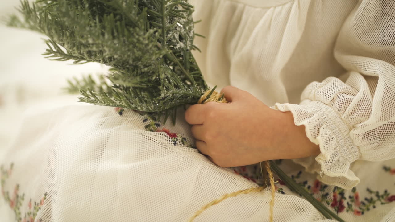 молодая девушка в белом праздничном платье держит ветку сосны с рождественским орнаментом - крупный план