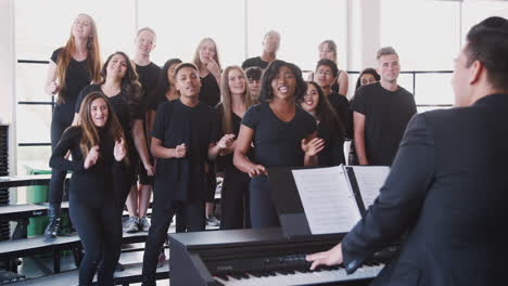 male and female students singing in choir with teacher at performing arts school