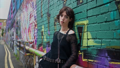 retrato de moda al aire libre de una mujer joven de estilo alternativo apoyándose en una pared cubierta de graffiti en la calle de la ciudad de londres, reino unido, en tiempo real.