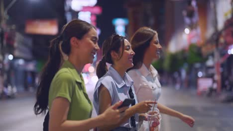 three young women walking at night in a city