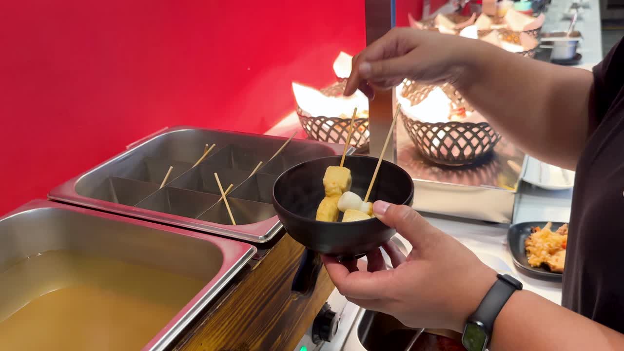 A vendor serves Korean oden skewers from a hot broth at a vibrant street stall in Bangkok, Thailand