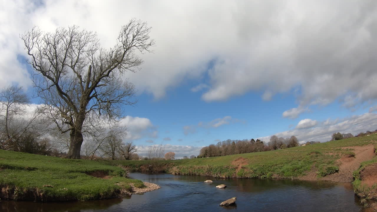 Una giornata soleggiata e ventosa sul fiume Arrow nel Warwickshire, Inghilterra, mentre le nuvole si addensano nel cielo.