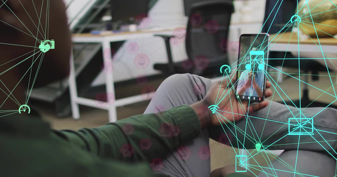 Seated man lifting smartphone toward camera in office animating holographic icons for business chat