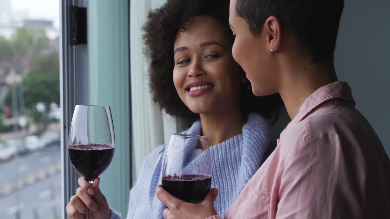 Lesbian couple drinking red wine at window