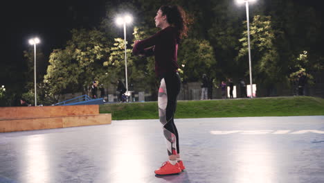 chica rizada deportiva estirando las piernas y haciendo estocadas en el parque por la noche