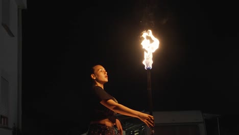 female fire eater at night, holding torch and blowing fuel on flame, slow motion