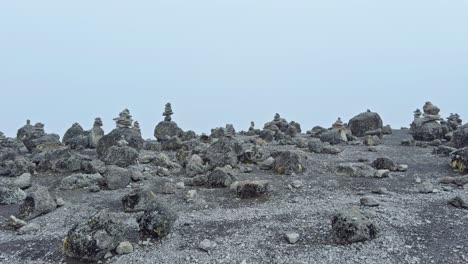 static ground-level shot shows numerous small rock cairns scattered across a barren rocky plain at high altitude on mount kilimanjaro, with a pale misty sky in the background